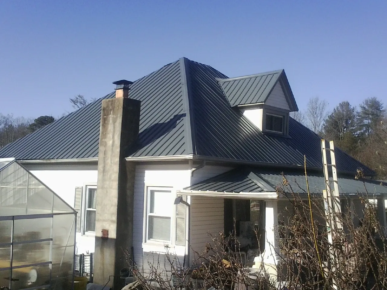 Dark blue standing seam metal roof on a white farmhouse with dormer — Slate & Tile Roof Repair by Roofing Brothers in New Lothrop