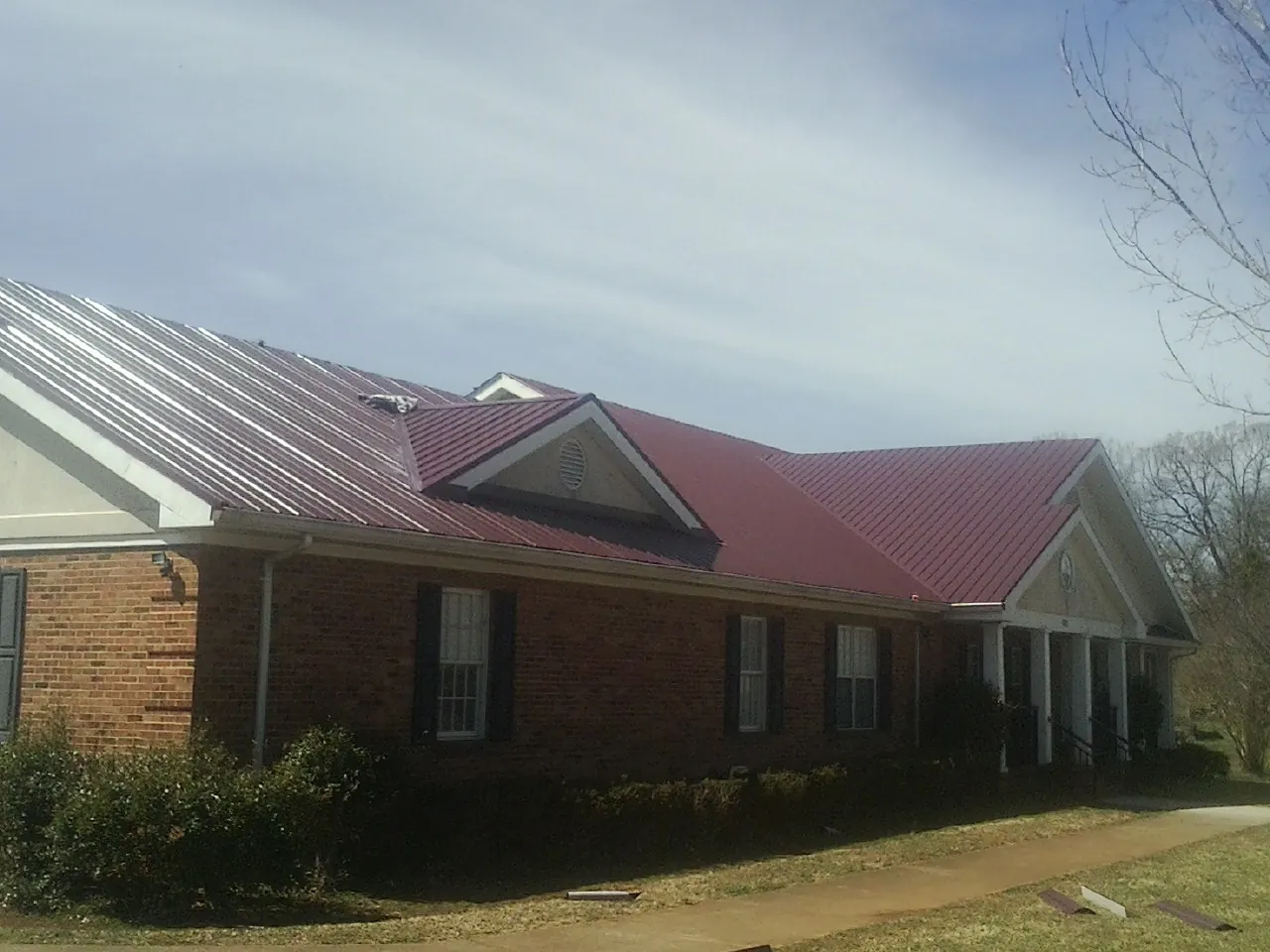 Red metal roof with gabled entries on a long brick building, from a Hail Damage Roof Repair job in New Lothrop