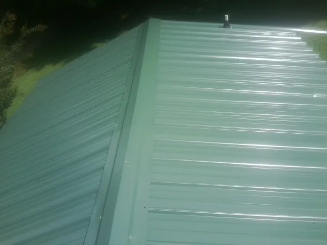 New green metal panels meeting at the ridge of a roof — Flat Roof Repair work by our crew in New Lothrop