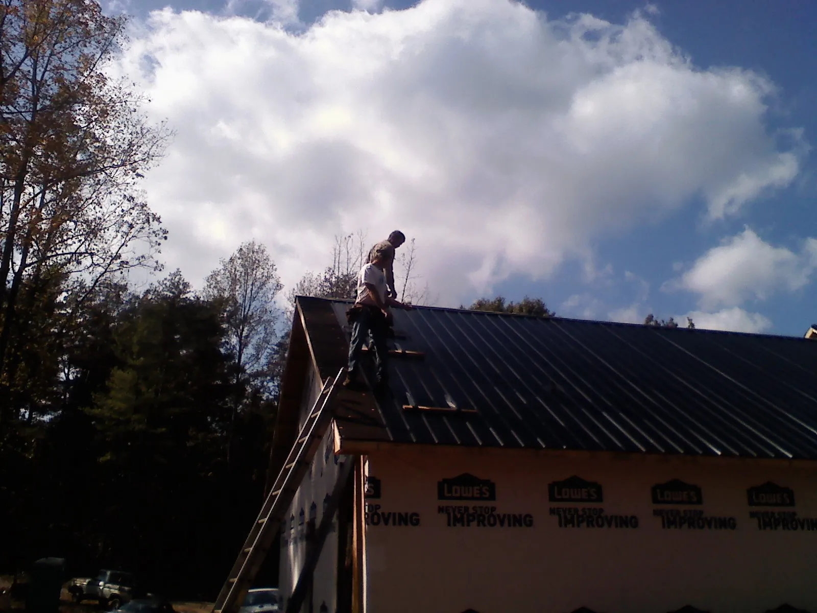 Roofer fastening dark metal panels high against a cloudy sky, from a Roof Inspection job in New Lothrop