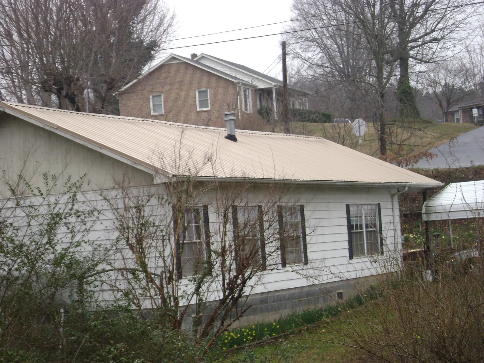 Tan metal roof on a white sided house set into a hillside — Commercial Roofing by Roofing Brothers in New Lothrop